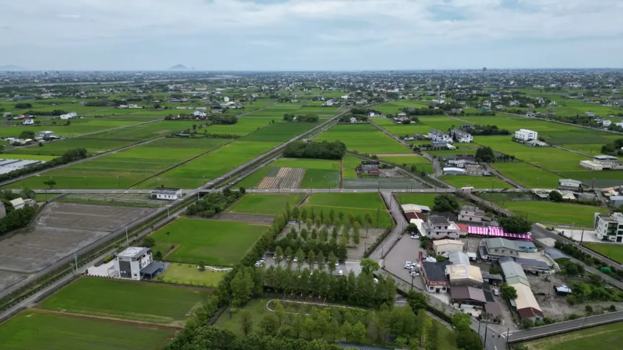 空拍台灣鄉間平原，綠色稻田之間散布著透天厝、農舍與道路，示意自地自建前要先確認土地的使用分區與使用地類別