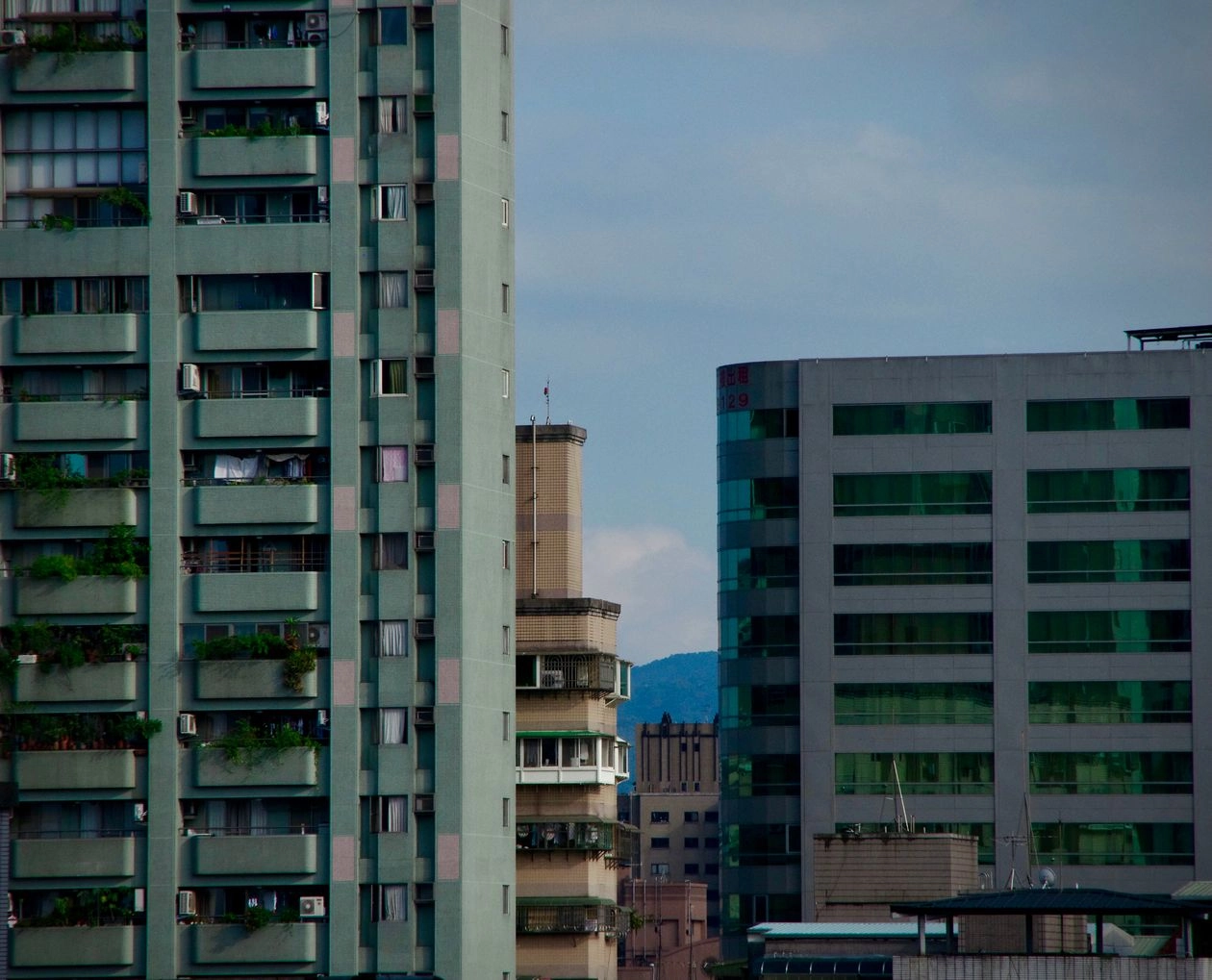 城市裡外牆陽台種滿植栽的高層住宅大樓，旁邊是玻璃帷幕辦公大樓，買地上權住宅前要先查清楚產權與剩餘年限