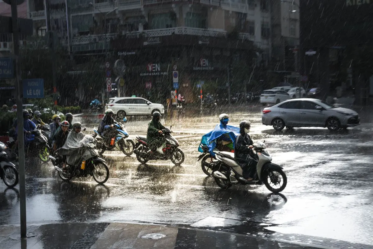 大雨中的十字路口,多名穿著輕便雨衣的機車騎士在積水路面上停等與前進,後方有汽車和街邊店家,像是豪雨特報期間的城市街景